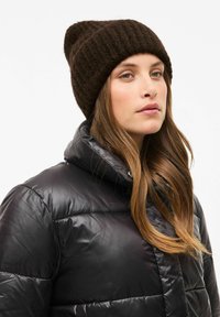 Gorro de punto marrón oscuro con textura acanalada, combinado con una chaqueta acolchada negra brillante que presenta un cuello alto y detalles de botones.