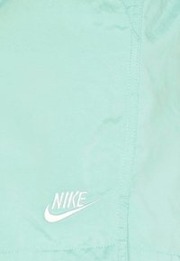 Veste légère vert menthe avec des coutures visibles et un logo Nike brodé en blanc. Texture lisse, design décontracté, sans motifs.