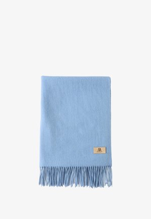 Châle bleu clair en tissu doux et texturé avec des bords à franges. Porté sur un pull beige, créant un look superposé.