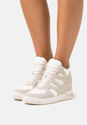 Baskets montantes beige présentant un mélange de cuir lisse et texturé, des accents blancs et un logo doré sur le talon. Conception à bout arrondi.