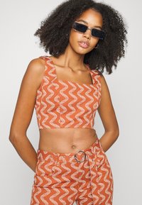 Top cropped laranja com decote quadrado, apresentando padrões ondulados brancos. O tecido parece texturizado, combinado com calças de cintura alta a condizer.