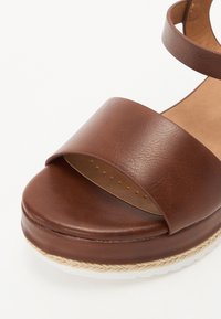 Brown leather platform sandal featuring a wide strap, an espadrille-style sole, and a smooth finish with circular perforations for breathability.