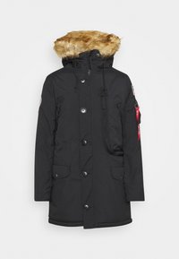 Parka d'hiver noir avec capuche doublée en fourrure, fermeture à boutons et zip devant, poches à rabat et une étiquette rouge sur la manche gauche.