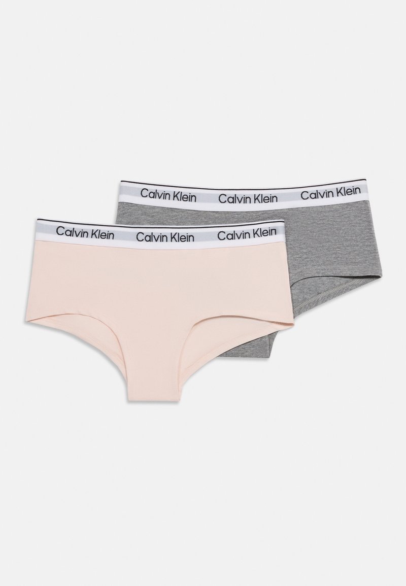 Dve ženski spodnji hlački hipsterskega stila, ena svetlo roza in ena siva, obe z belim elastičnim pasom z blagovno znamko "Calvin Klein".
