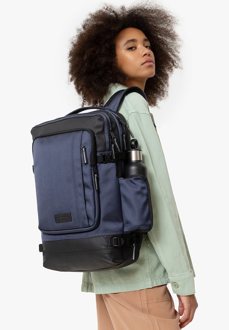 Mochila azul marino con tela texturizada, acentos negros, múltiples compartimentos, soporte para botella de agua y correas acolchadas para mayor comodidad.