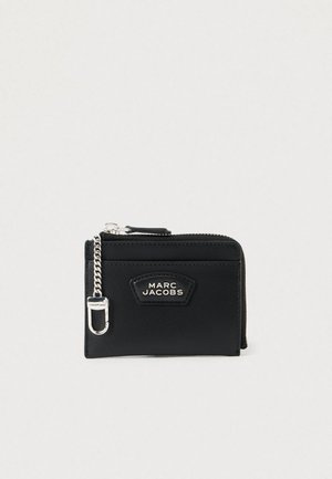 Portafoglio in pelle nera con chiusura a zip, dettaglio in catena argentata e patch con logo frontale. Design compatto, texture minimale.