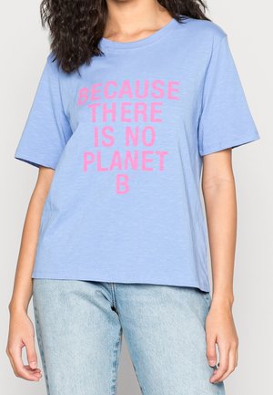 Osoba nosząca jasnoniebieską koszulkę z różowym napisem „Because there is no Planet B” oraz jasnoniebieskie dżinsy.