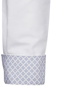 Manica di un cappotto da chef bianco con un polsino a motivi blu e bianchi, caratterizzato da un design floreale geometrico e un tessuto a superficie liscia.