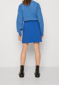 Niebieski sweter z dzianiny z bufiastymi rękawami, zestawiony z jednolitym niebieskim mini spódnicą i czarnymi botkami za kostkę. Gładka faktura, casualowy styl.