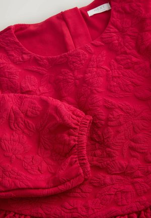 Raudonas gėlių raštais dekoruotas suknelės viršus, pagamintas iš tekstūruoto audinio, su lygiu iškirpimu ir elastingais rankogaliais. Uždarymas užtrauktuku nugaros pusėje.