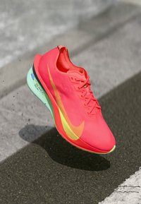 Rode sportieve schoen met een bovenkant van gaas, gele swoosh-accent en een muntgroene zool. Beschikt over veters, een ronde neus en een getextureerd oppervlak.