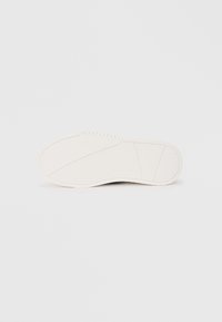 White sneaker sole with a textured surface, featuring grooves for traction and a subtle brand logo embossed on the side.