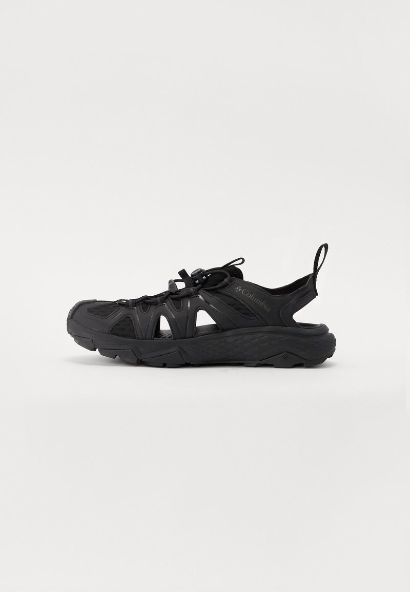 Sapatos atléticos pretos com painéis em malha, sola texturizada e atacadores ajustáveis. Apresenta uma alça na parte traseira para facilitar o calçar.