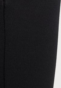 Svarta ribbade leggings tillverkade av elastiskt tyg, med en texturerad yta och vertikala linjer, samt en sömlös design längs sidorna.