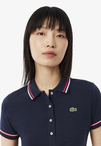 Navy blue cotton polo shirt with a solid design, featuring a red and white striped collar and sleeves, and a small embroidered crocodile logo.