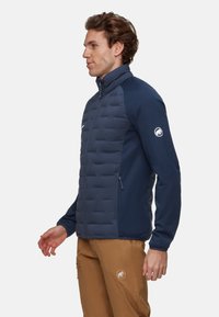 Marinejakke med polstret front, glatte ærmer, høj krave og lynlåslommer. Designet til fleksibilitet og varme.