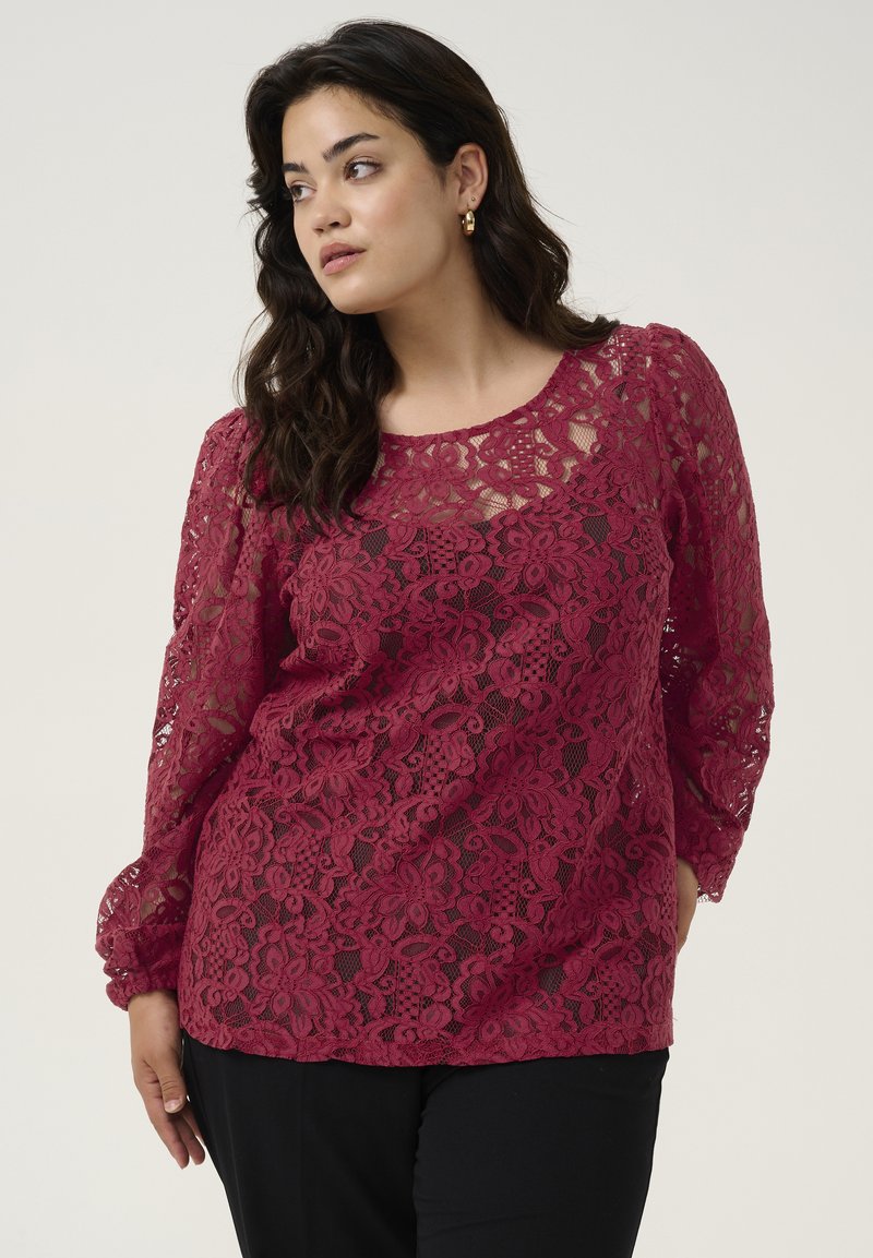 Top din dantelă bordeaux cu mâneci lungi, modele florale și guler rotund. textilele sunt transparente cu un finisaj texturat.
