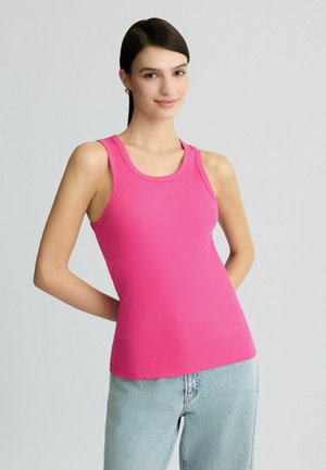 Débardeur rose côtelé avec décolleté en U et détail de logo brodé. Assorti avec un jean bleu clair, mettant en valeur une coupe ajustée.