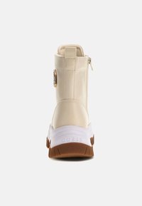 Sneaker alta beige con finitura lucida, dotata di suola in gomma bianca, dettagli in metallo dorato e zip laterale per indossarla facilmente.