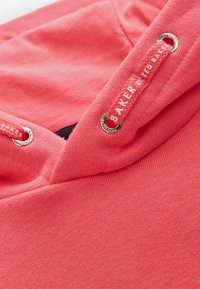 Felpa corallo con una texture morbida, dotata di occhielli in argento e di un laccio rosso con etichetta "BAKER by TED BAKER."