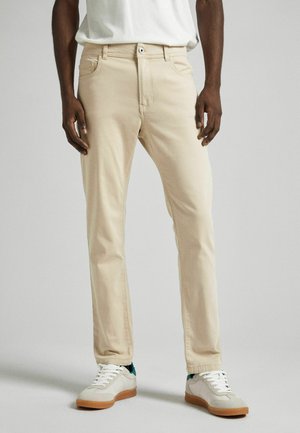 Beige Gerade-Passform-Hosen aus Baumwollmischung, mit Reißverschluss und fünf Taschen, getragen mit weißen und grünen Sneakers.