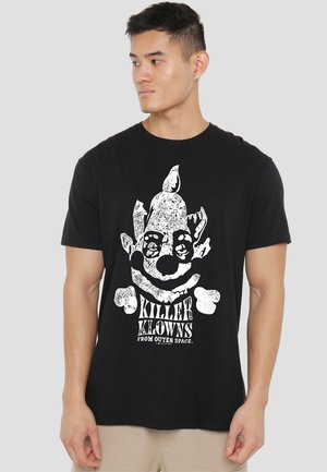 Black t-shirt featuring a white graphic print of a clown with crossed bones and "KILLER KLOWNS FROM OUTER SPACE" text below. Short sleeves.