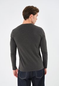 Langmouw, donkergrijze T-shirt, ronde hals, getailleerd ontwerp, gladde textuur, gecombineerd met donkerdenimspijkerbroek met zichtbare stikdetails.