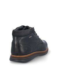 Botín negro de cuero hasta el tobillo con una textura lisa, punta redondeada, cuello acolchado y una suela de goma marrón en contraste. Detalle sutil de marca visible.