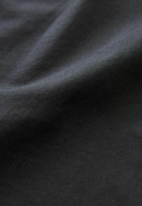 Gładka czarna tkanina z delikatnymi fałdami, ukazująca drobną fakturę i miękkie matowe wykończenie pod delikatnym oświetleniem.