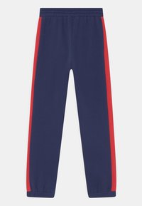 Marineblaue Jogginghose mit roten Seitenstreifen, elastischem Bund und elastischen Bündchen. Aus weichem Stoff gefertigt, mit einem geraden Bein-Design.