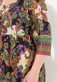 Multikleurige jurk met paisleypatroon op een zwarte achtergrond, met een vierkante halslijn en ellebooglange mouwen met decoratieve accenten.