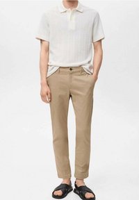 Bílá texturovaná polo košile s krátkým rukávem, béžové slim-fit chino kalhoty a černé sandály s křížovým páskem.