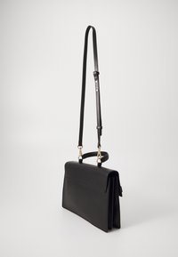 Geantă de mână din piele neagră cu capac pliat, curea ajustabilă și accesorii de culoare aurie. Prezintă o textură netedă și un design minimalist.