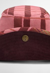 Chapéu de balde em padrão xadrez rosa e bordô, com textura em corduroy e etiqueta em logo dourado. A seção superior é padronizada, enquanto a inferior é sólida.
