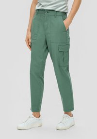 Grüne Baumwoll-Cargohosen mit slim Fit, ausgestattet mit Seitentaschen, einem Knopfverschluss und hochgekrempelten Säumen, kombiniert mit weißen Sneakers.