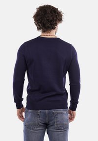 Maglione lavorato a maglia blu navy con polsini e orlo a coste, presenta un collo a giro e viene abbinato a jeans di denim blu.