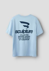 T-shirt en coton bleu clair avec un grand graphisme bleu foncé au dos. Le texte indique : "sculpture COLLECTIVE APPAREL EDITION POUR LE PEUPLE DE DEMAIN."