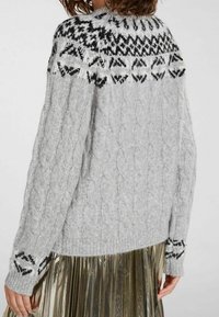 Grå kabelstickad tröja med en yoke i svartvitt mönster med paljettaccent, texturerade ärmar och ribbade muddar, bärs över en plisserad kjol.