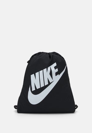 Sort snøresæk med stort hvidt Nike-logo og swoosh foran, sat mod en ensfarvet lys baggrund.