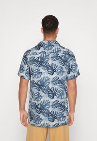 Camicia a maniche corte di colore azzurro chiaro con motivo di foglie tropicali blu scuro, dotata di colletto e vestibilità comoda. Realizzata in tessuto leggero.