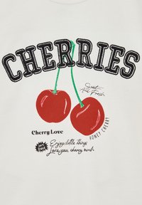 Balta marškinėliai su ryškiu juodu užrašu "KINGSTUOMEN." Viršuje yra du siuvinėti raudoni vyšnios su žalios stiebais, o žemiau - žaismingas tekstas ir akcentai.