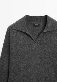 Grå strikket sweater med V-hals og krave. Blød tekstur og ribbede manchetter. Mærke synligt indeni kraven.