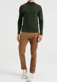 Green knit turtleneck sweater, fitted design, paired with casual brown trousers and light-colored sneakers. Textured fabric, ribbed cuffs.