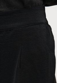 Κο ντινό πλάνο στη μέση και στην πλαϊνή τσέπη μαύρου παντελονιού με εμφανείς ραφές στο ύφασμα.