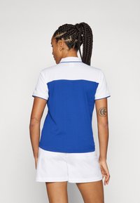Blau-weißes Poloshirt mit strukturiertem Muster, kurzer Ärmel, klassischem Kragen und kontrastierender blauer Borte an den Kanten.