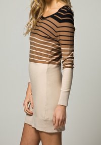 Robe en maille à rayures horizontales dans des tons marron, avec une partie inférieure unie beige. Elle est dotée de manches longues et d'une silhouette ajustée.