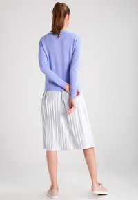 Jasnofioletowy sweter dzianinowy z długimi rękawami, zestawiony z białą plisowaną spódnicą midi i różowymi trampkami. Projekt posiada okrągły dekolt.