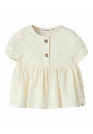 Blouse bébé couleur crème à manches courtes, œillets floraux brodés, deux boutons en bois sur la patte de boutonnage avant et détail froncé à la taille.