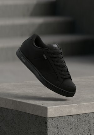 Črne superge iz gladkega usnju podobnega materiala, s perforiranimi stranskimi paneli, ravnimi vezalkami in gumijastim podplatom. Na strani je viden logotip Etnies.