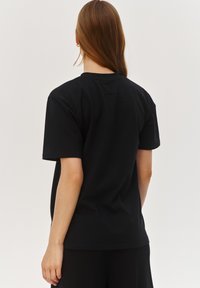Czarny bawełniany t-shirt z krótkimi rękawami, okrągłym dekoltem i luźnym krojem; gładka faktura z prostym, nieozdobionym wzorem.